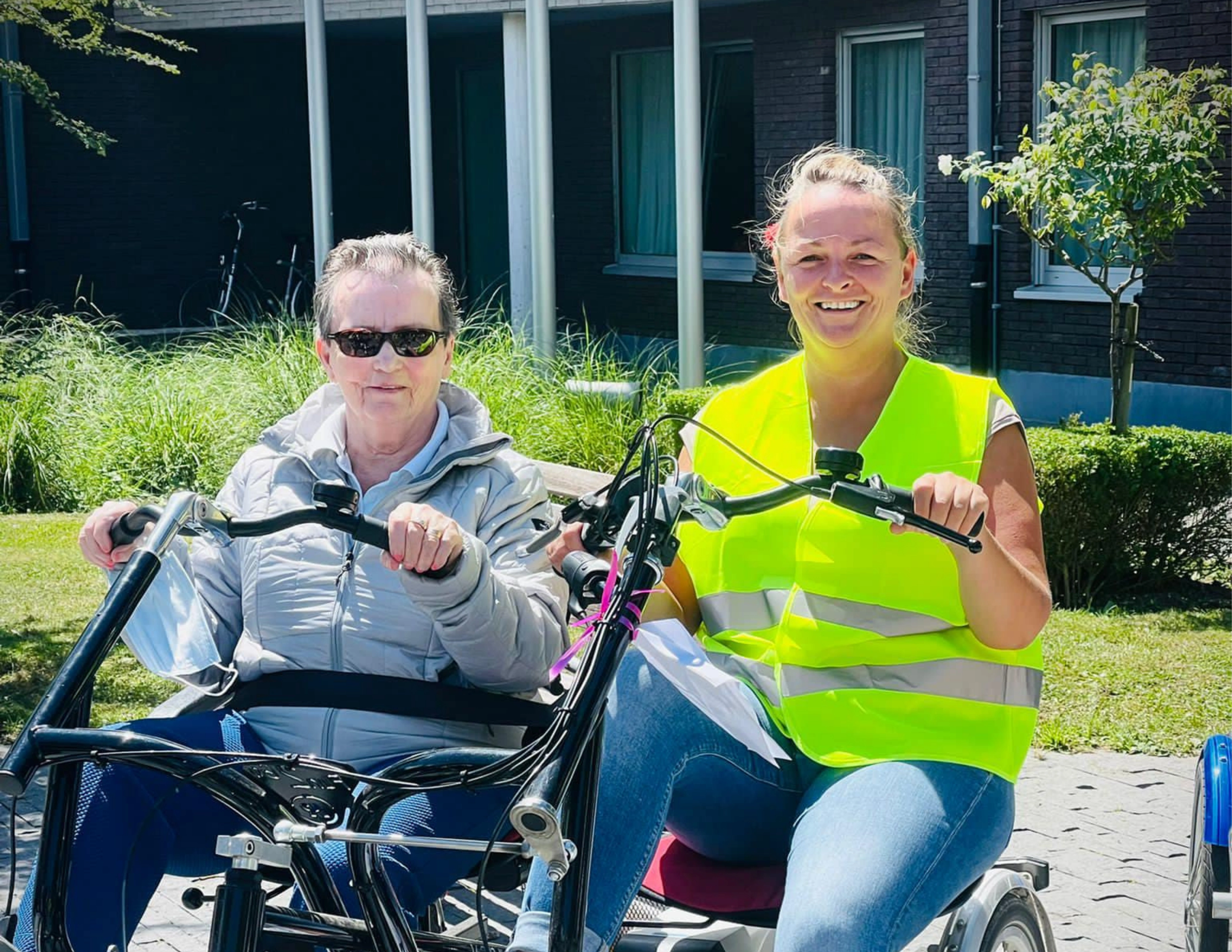 Vrijwilliger en bewoonster zitten op de fiets en lachen naar de camera