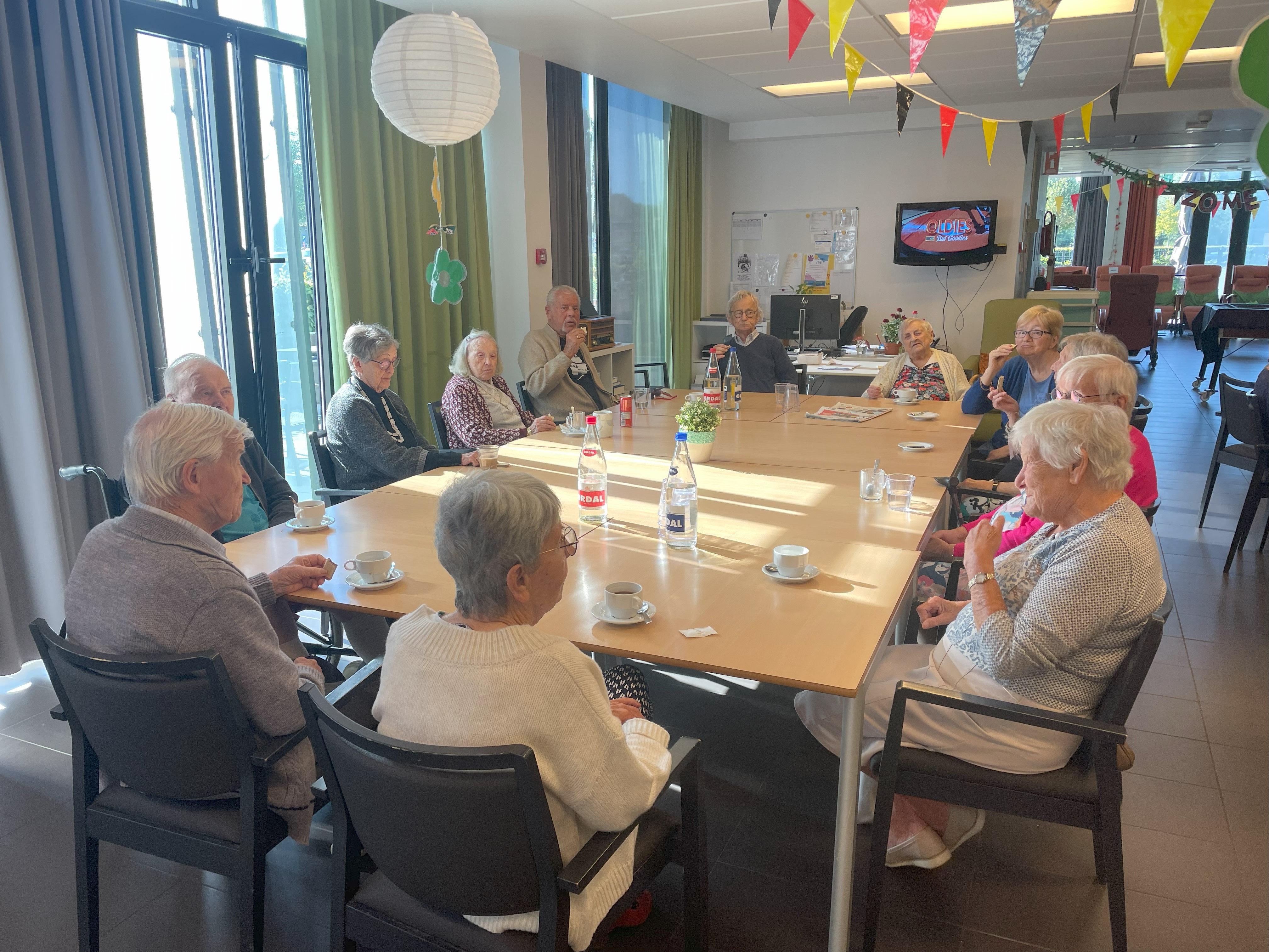 Volle tearoom met vlaggetjes en bewoners rond de tafel