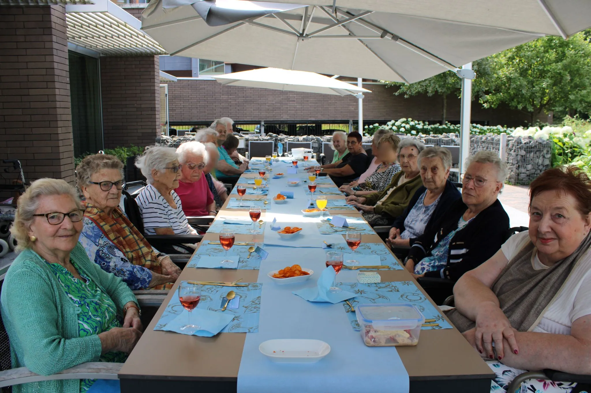 Bewoners zitten buiten aan een terras met drankjes op tafel