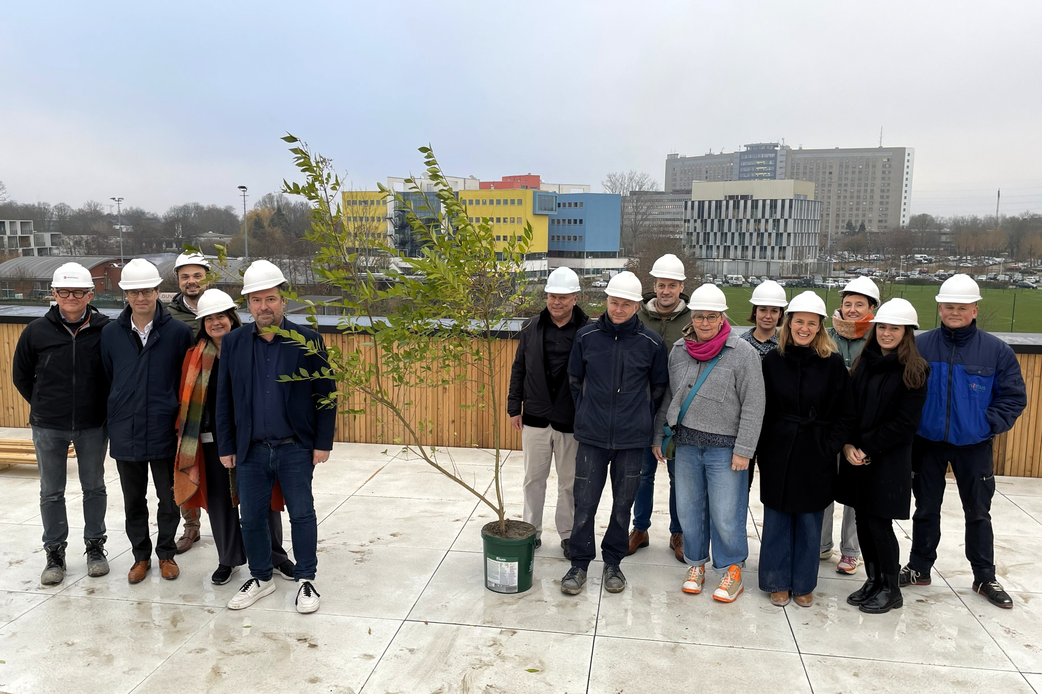 Voorzitter Pablo Annys poseert samen met leden van Ruddersstove en de technische dienst van Mintus bij de Meiboom op het dak van het bouwproject.