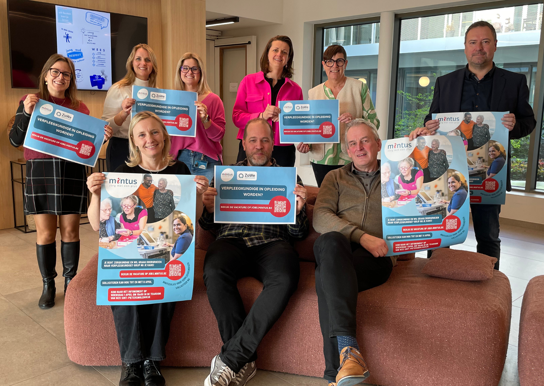 Collega's van Mintus poseren samen met voorzitter Pablo Annys (foto rechts) terwijl ze elk een affich van het project Mintus-klas vasthouden.