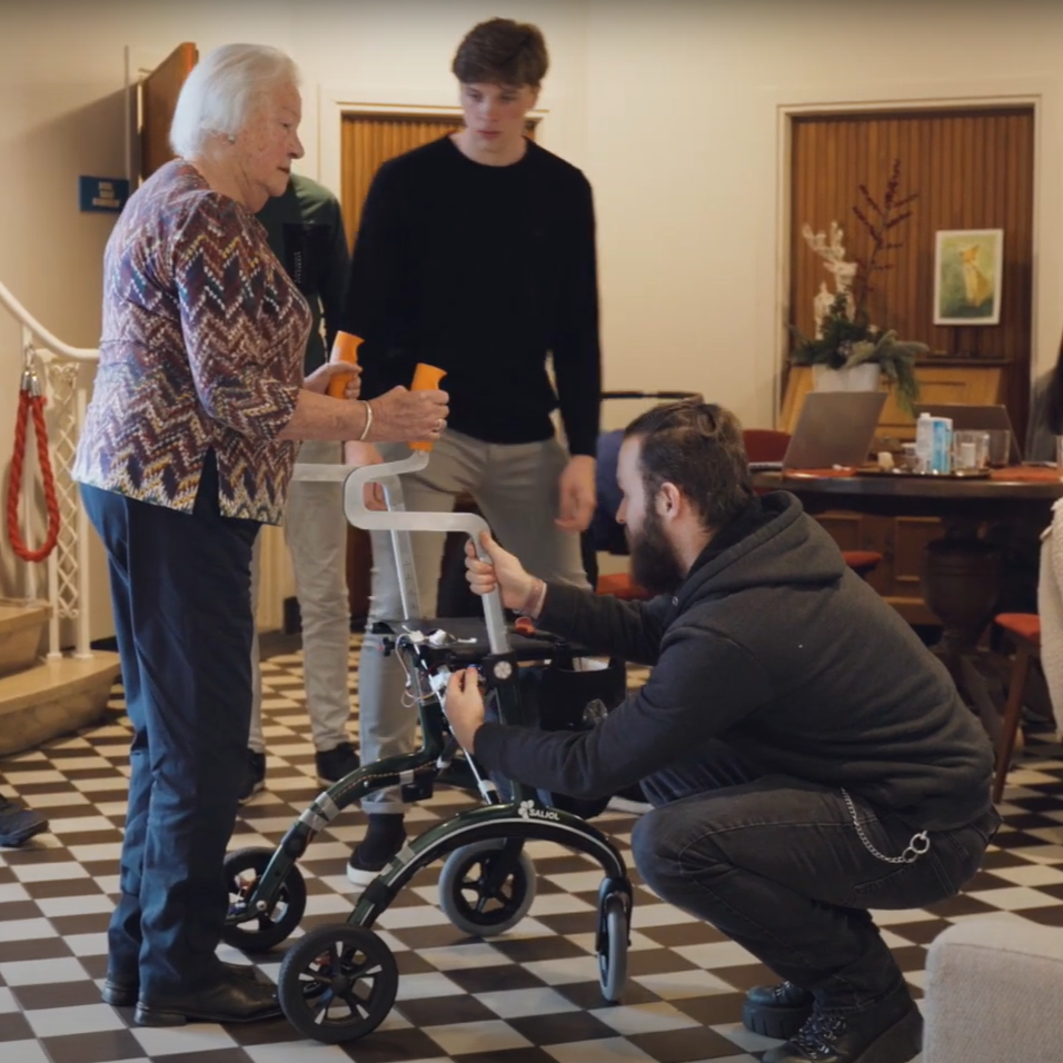 Twee medewerkers van Breda Robotics stellen de geavanceerde rollator af van een oudere dame.
